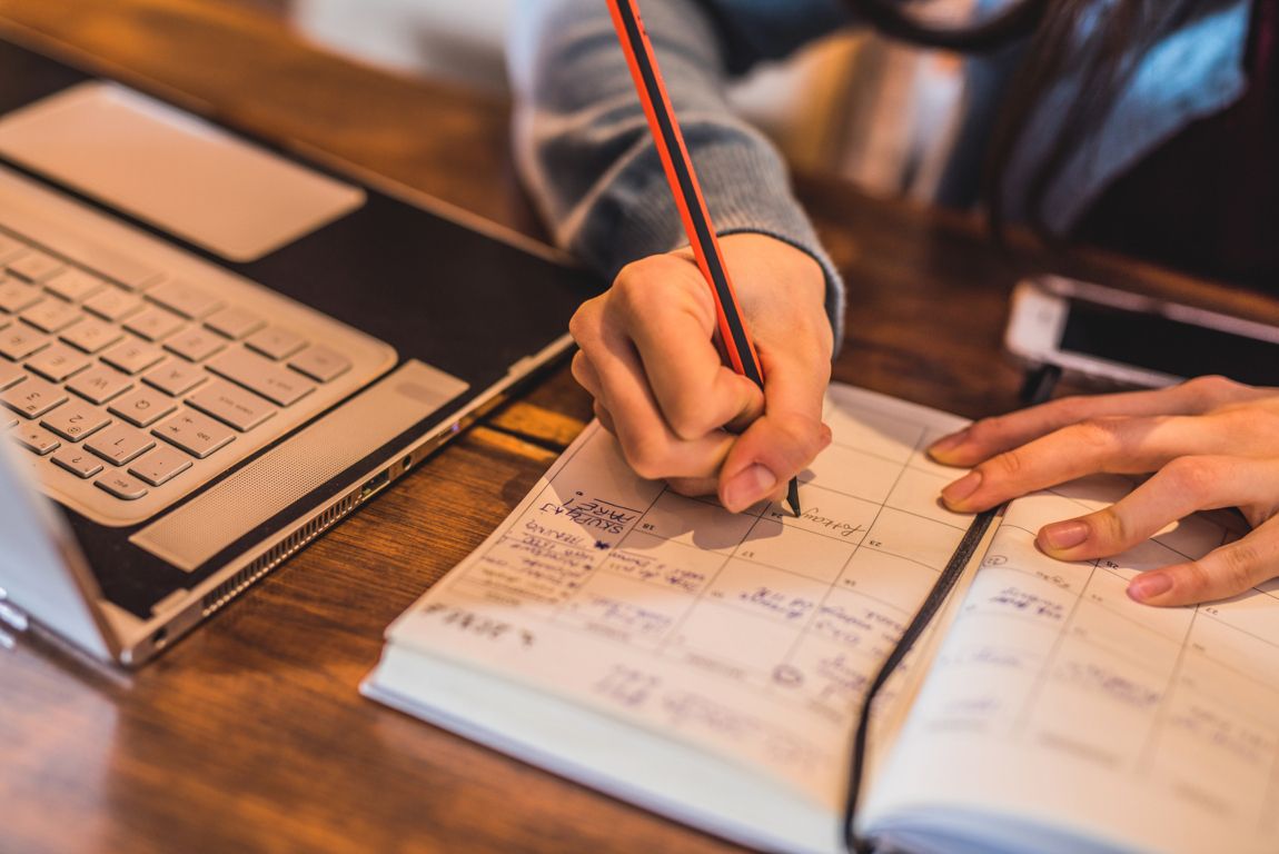 Mano escribiendo en una libreta, apuntando el calendario de finanzas personales para el 2025