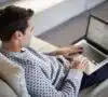 Hombre con un portátil en las piernas haciendo la declaración de la renta este 2025