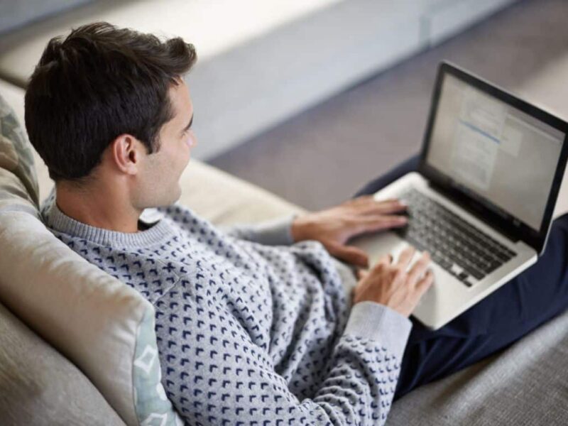 Hombre con un portátil en las piernas haciendo la declaración de la renta este 2025