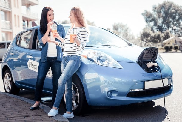 Chicas cargando un coche sostenible mientras hablan