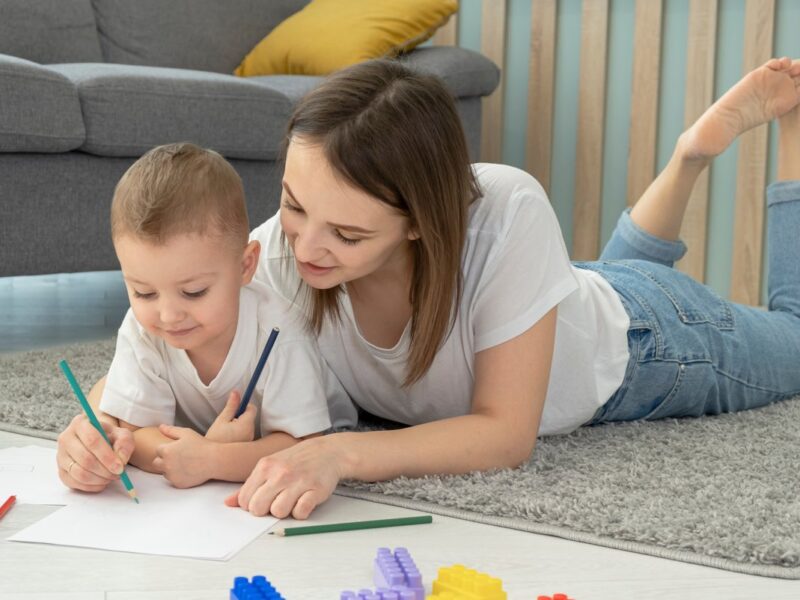 Familia monoparental de mamá e hijo dibujan tumbados en el suelo de su casa.