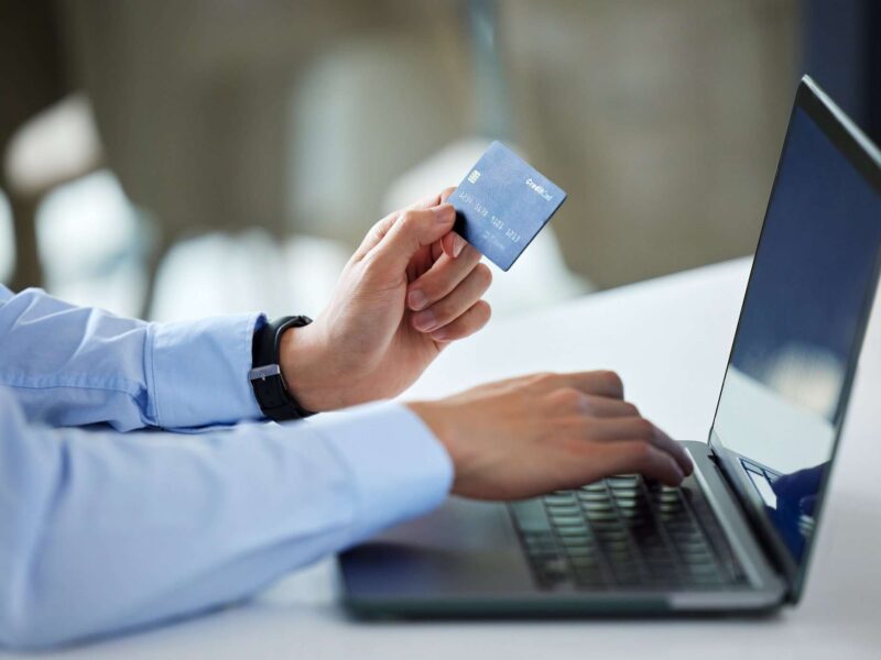 Hombre mirando en el ordenador, con tarjeta en mano, comprando en una tienda online segura