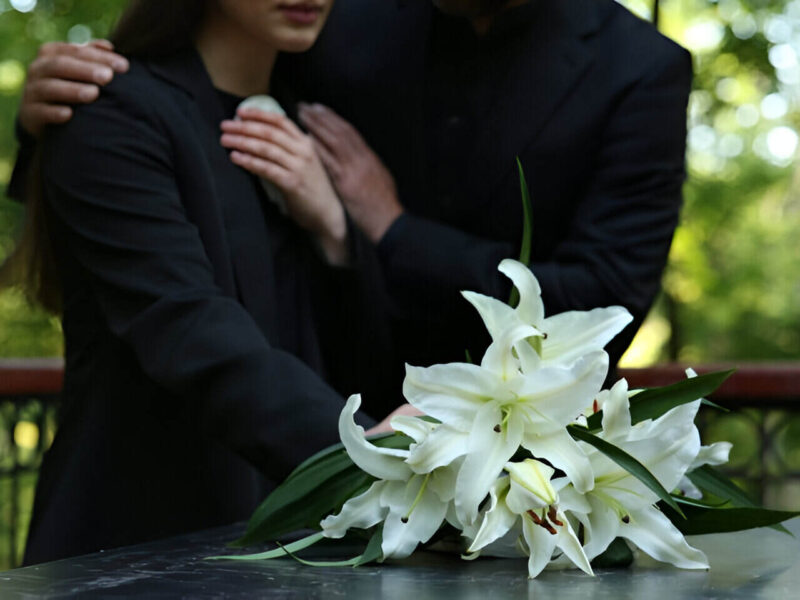 Mujer y hombre de luto, abrazándose frente a un ataúd, preguntándose cuánto cuesta un entierro