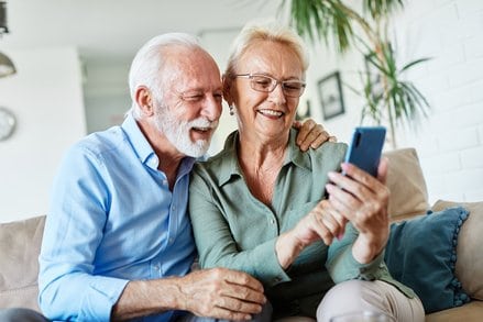 Una pareja de personas mayores observan un móvil mientras sonríen, viendo las ofertas que hay para la economía plateada