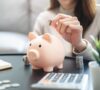 Manos de una mujer metiendo monedas en una hucha de cerdo, luego de ahorrar al descubrir las ciudades más baratas para vivir en España
