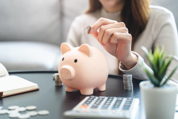 Manos de una mujer metiendo monedas en una hucha de cerdo, luego de ahorrar al descubrir las ciudades más baratas para vivir en España