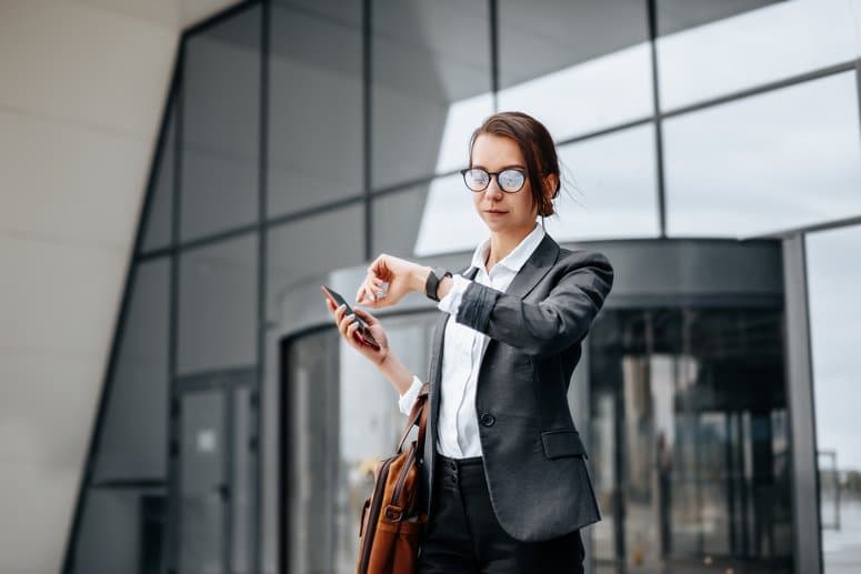 Mujer observando su reloj a la salida del trabajo, cumpliendo con la reducción de la jornada laboral en España