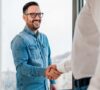 Hombre con camisa azul estrechando la mano de otra persona tras hacer un contrato entre familiares