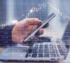 Doble exposición de las manos de una persona con un teléfono, un ordenador y un gráfico financiero