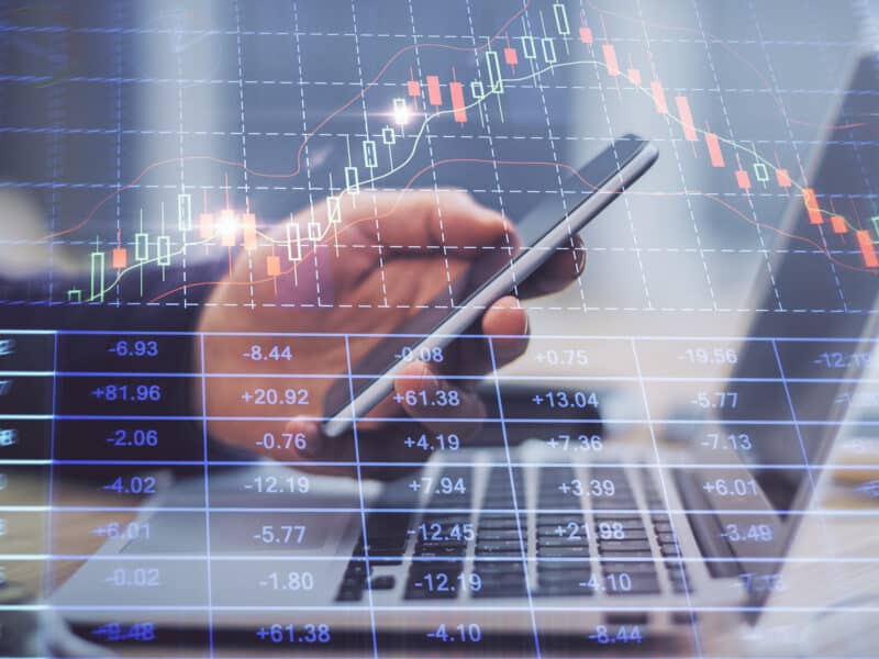 Doble exposición de las manos de una persona con un teléfono, un ordenador y un gráfico financiero